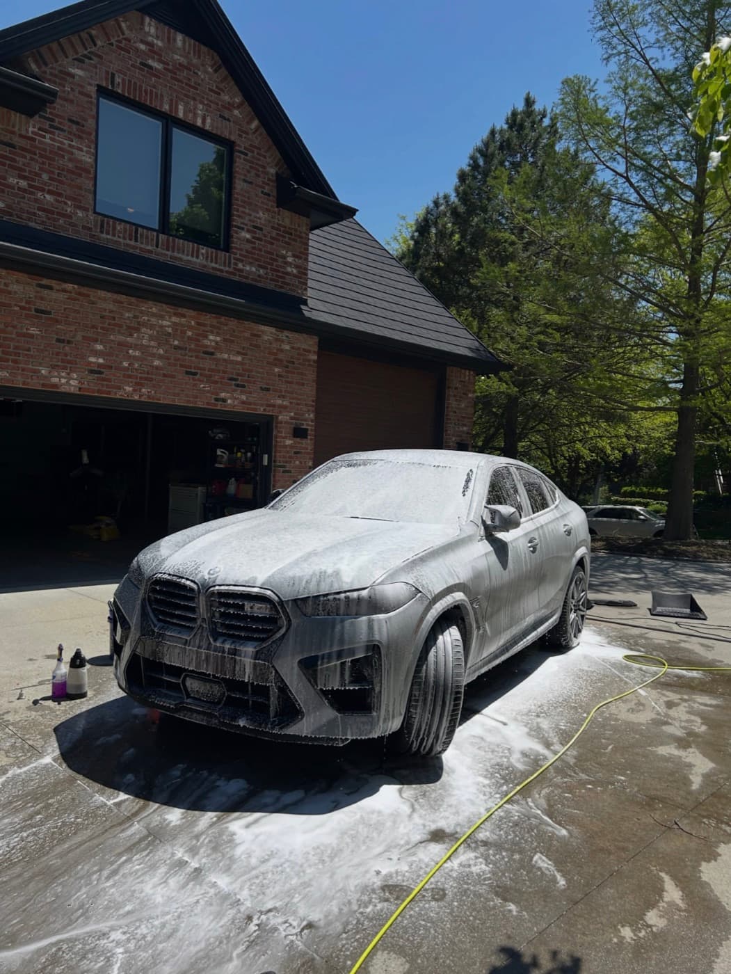 BMW X6 covered in pre-wash foam during a mobile exterior detail in a residential driveway